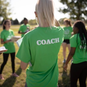 Two Girls on the Run junior coaches sit with their backs to the camera in green shirts talking to each other