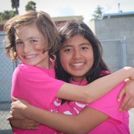 Smiling Girls on the Run participant hugging another smiling participant from behind