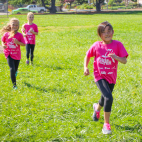 Two Girls on the Run participants smile at the camera while running at an outdoor practice in yellow shirts
